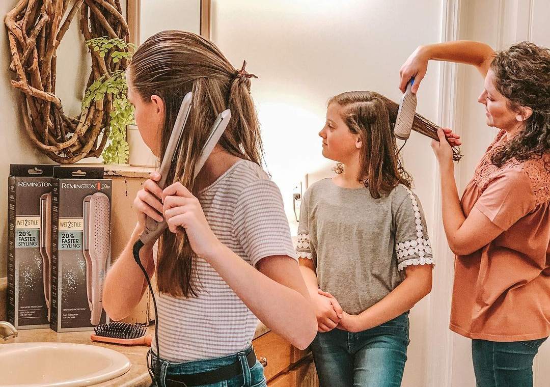 2 girls using flat iron to straighten wet hair